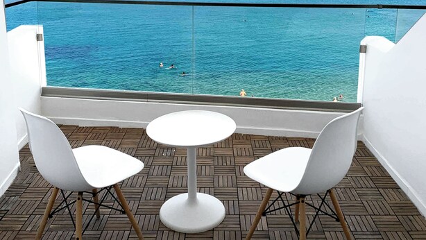 Un balcon avec vue sur l’océan, comprenant deux chaises blanches et une petite table ronde.