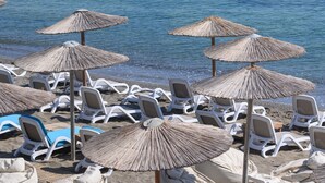 Une plage bordée de rangées de chaises longues blanches et de parasols en paille, avec vue sur la mer.