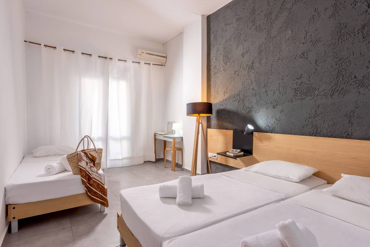 A hotel room with two beds, a desk, a chair, a lamp, and a large textured wall.