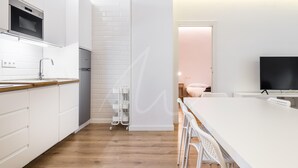 A modern kitchen with white cabinetry, a wooden countertop, and a built-in oven. There is a white dining table with chairs in the adjacent room. - Saboredo (Baqueira)