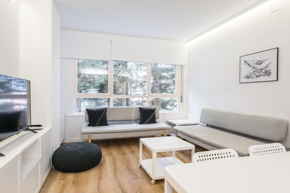 Una sala de estar moderna con un sofá, un reposapiés y un televisor sobre un mueble.