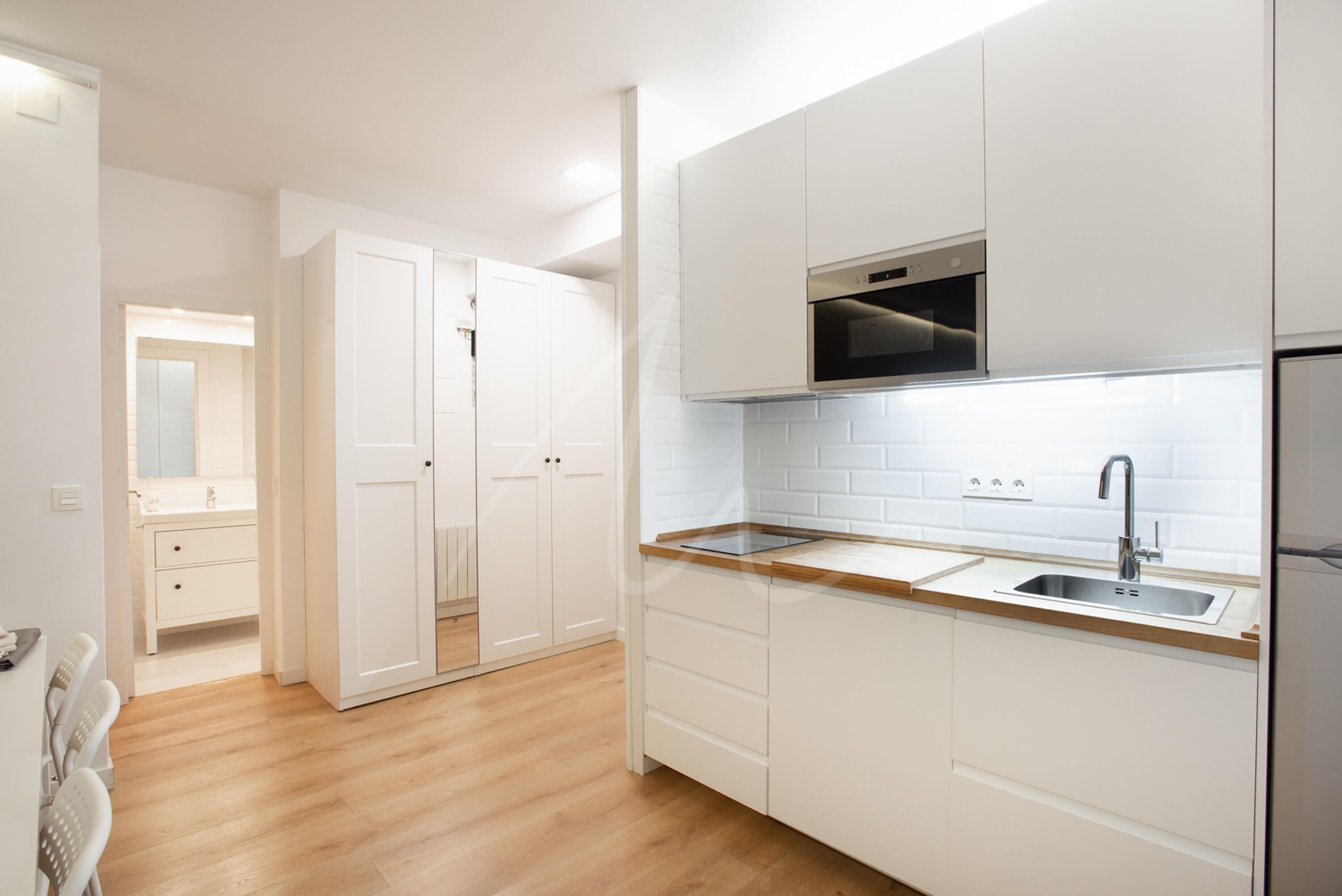 A modern kitchen with white cabinetry, a wooden countertop, and a stainless steel sink.