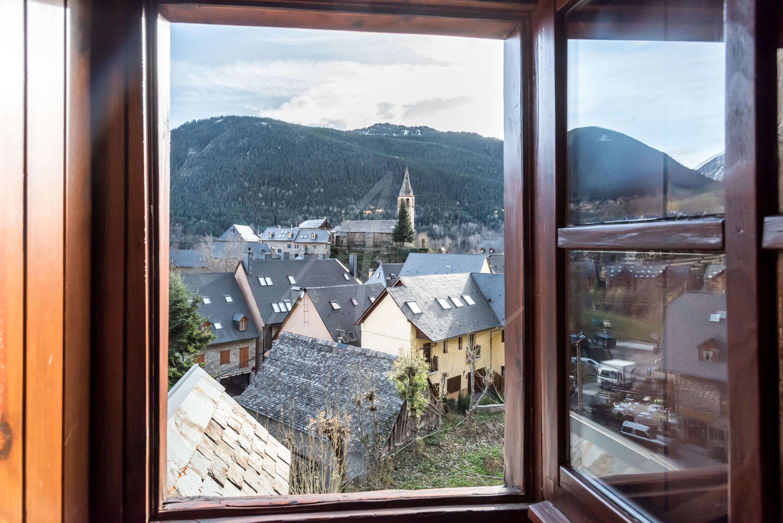 A view from a window of a town with a church, houses, and mountains in the background.