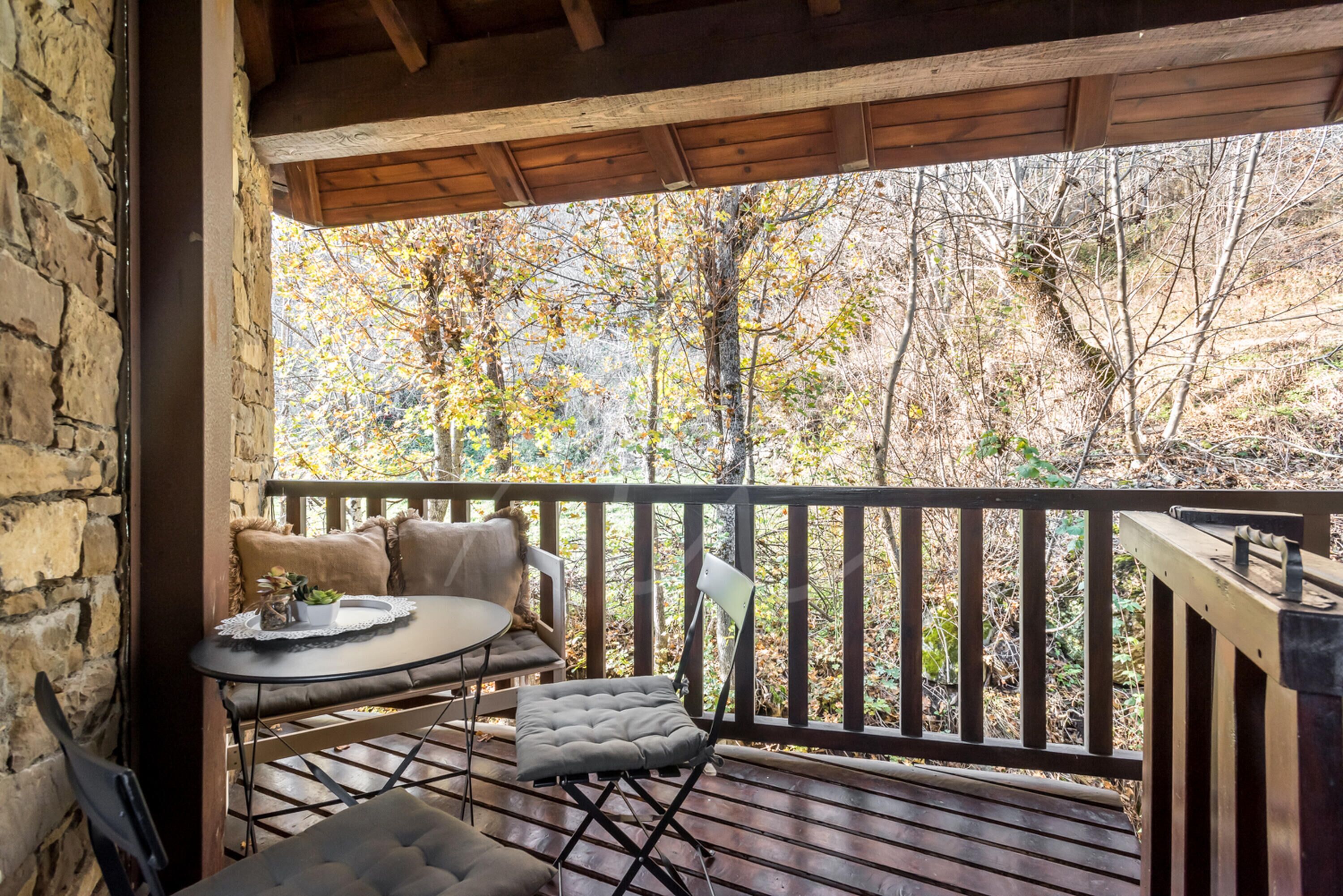 Una terraza de madera con mesa y sillas, con vistas a un área boscosa.