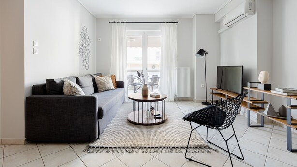 A modern living room with a sofa, coffee table, and a chair. There is a TV and a bookshelf. - Ideal 1 BR Apartment in Petralona (Athens)