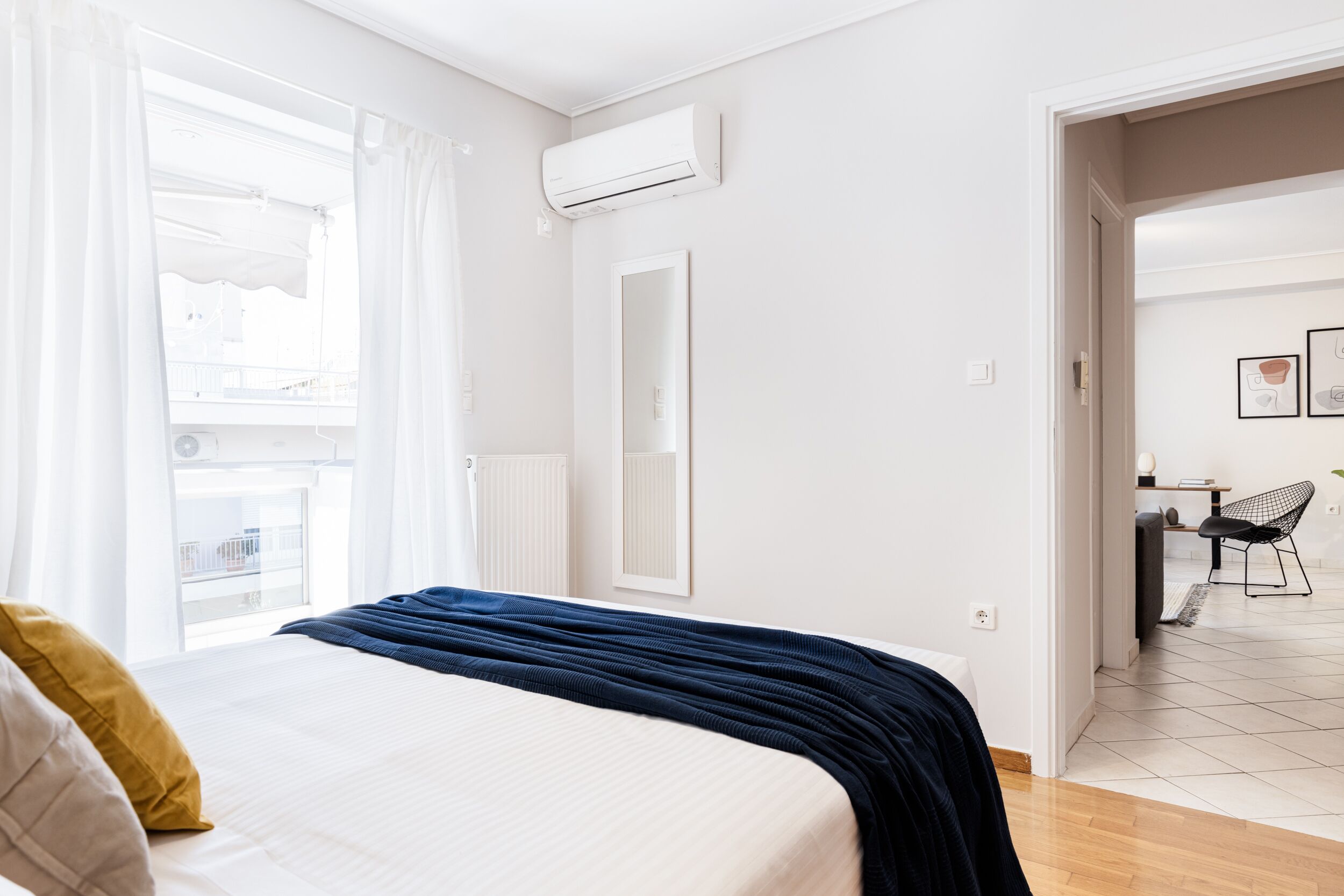 Habitación de hotel con cama, ventana con cortinas, equipo de aire acondicionado, espejo y vista a un balcón.