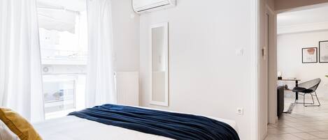 Habitación de hotel con cama, ventana con cortinas, equipo de aire acondicionado, espejo y vista a un balcón.