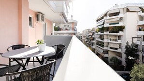 A balcony with a round table and chairs, overlooking a residential area with multi-story buildings. - Ideal 1 BR Apartment in Petralona (Athens)