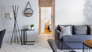 A modern living room with a grey sofa, a small side table with a plant, a black wire chair, and a wooden coffee table. - Ideal 1 BR Apartment in Petralona (Athens)