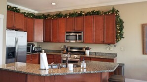 Une cuisine avec des meubles en bois, des plans de travail en granit, des appareils électroménagers en acier inoxydable et une guirlande de Noël.