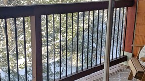 Une terrasse en bois avec une rambarde en métal, une chaise Adirondack en bois et une table avec un ventilateur.