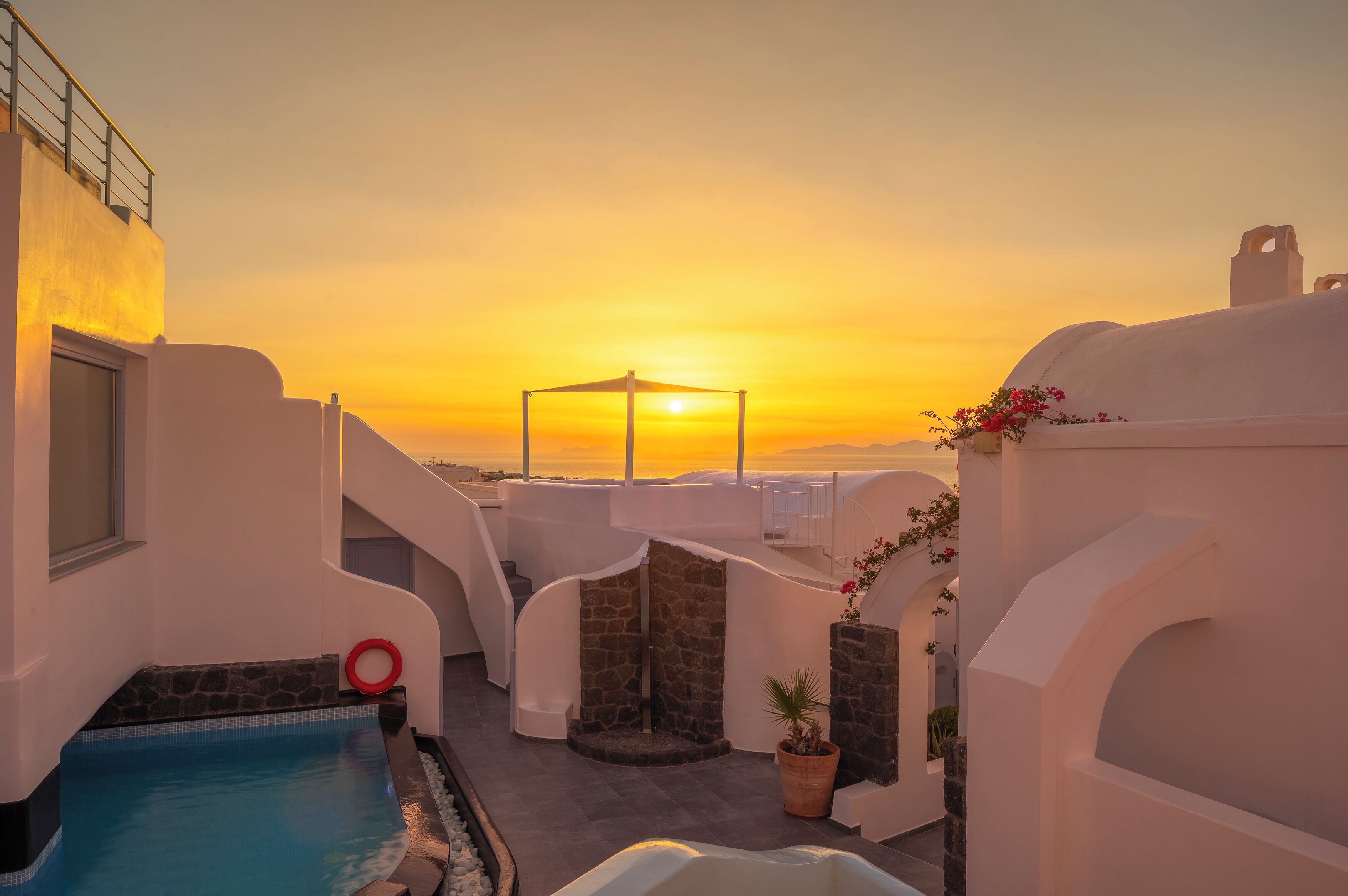 A rooftop pool area with a sunset view, stone walls, and a small garden with flowers.
