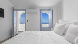 Un dormitorio con una cama grande, dos puertas que dan a un balcón y un televisor montado en la pared.