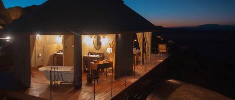 Une cabane moderne et bien éclairée, dotée d’une grande baignoire, d’une terrasse en bois et offrant une vue sur le paysage environnant.