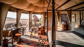 A tented room with a desk, chairs, a bed, and a view of the desert. - Zannier Sonop (Sesriem)