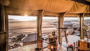 Una habitación con tienda de campaña, un escritorio de madera, una silla y vistas a un paisaje desértico.
