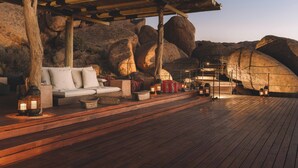 An outdoor seating area with a wooden deck, white sofa, and lanterns. - Zannier Sonop (Sesriem)