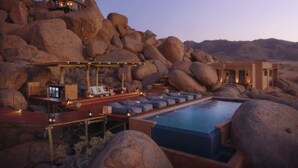 A luxurious outdoor pool area with large rocks, a wooden deck, and a pool. - Zannier Sonop (Sesriem)