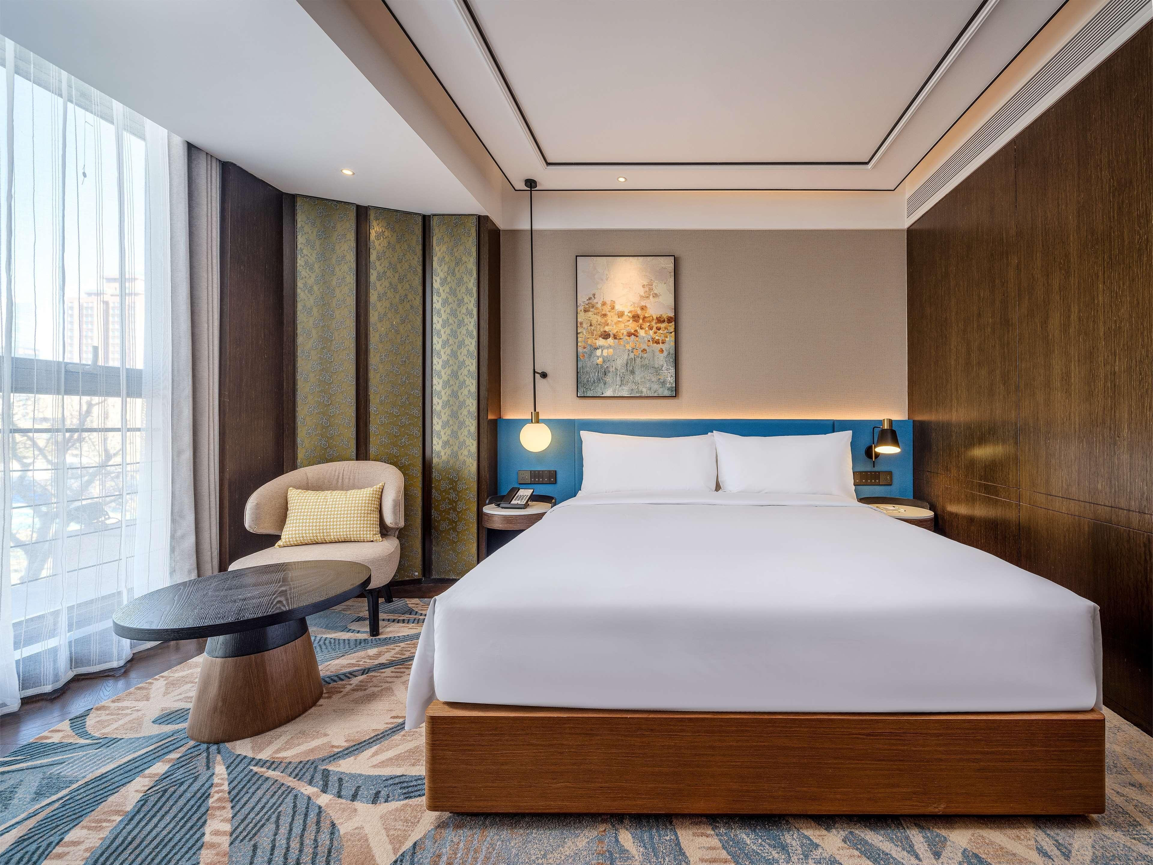 A hotel room with a large bed, a chair, a small table, and a view of the city.