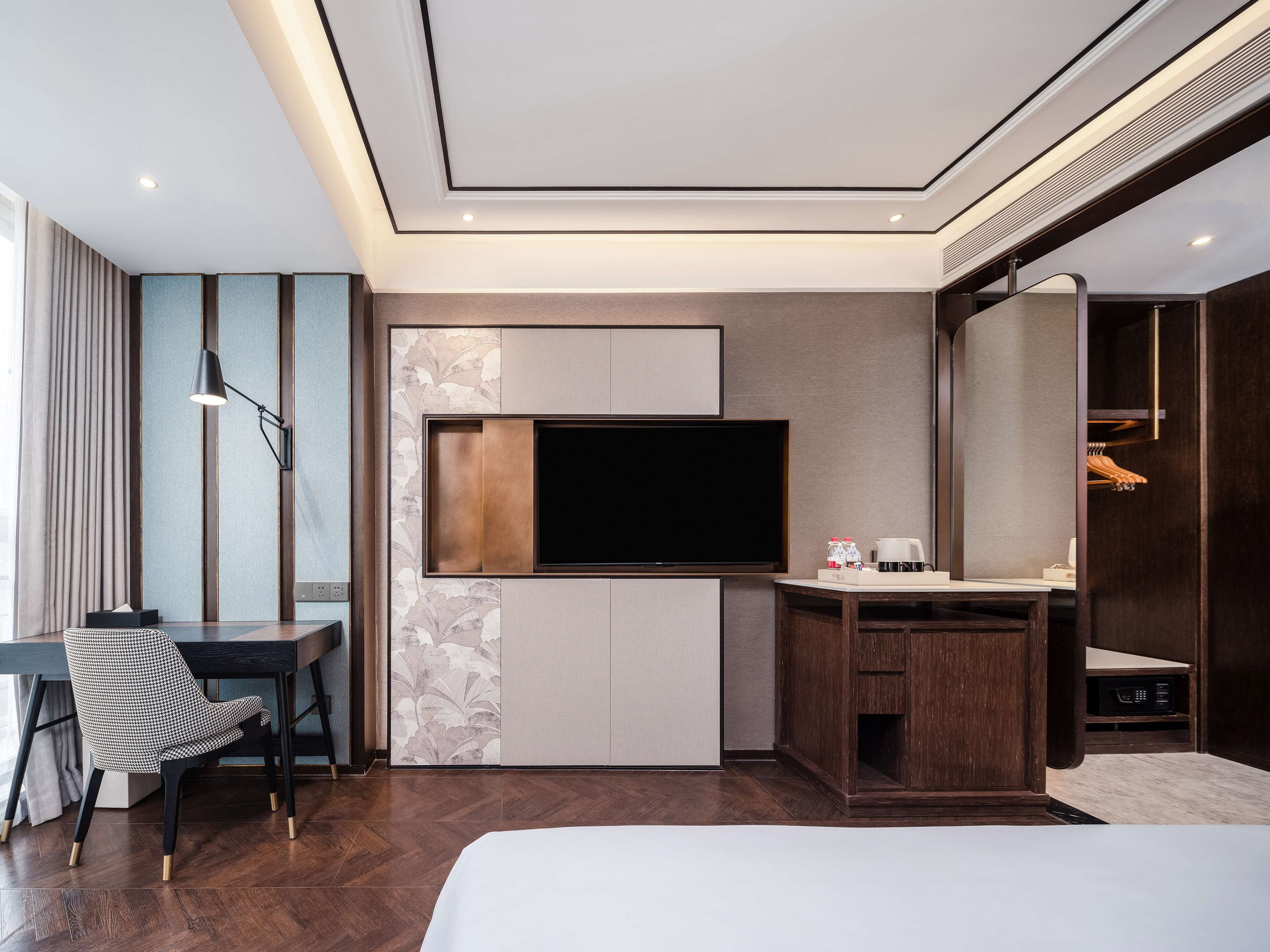 Quarto de hotel moderno com cama, escrivaninha, televisão de tela plana, guarda-roupa e espelho.