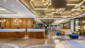 Um hall de hotel moderno com balcão de recepção, área de estar e piso de mármore curvo.