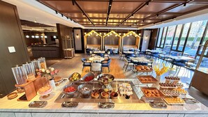 Uma área de buffet com diversos alimentos e um espaço de refeições com mesas e cadeiras.