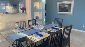 A dining area with a table set for four, chairs, a vase with red flowers, and a framed painting on the wall. - 7BR Family & Spacious Group Retreat!  Sleeps 14! Private Pool! 15 Min to Disney! (Kissimmee)