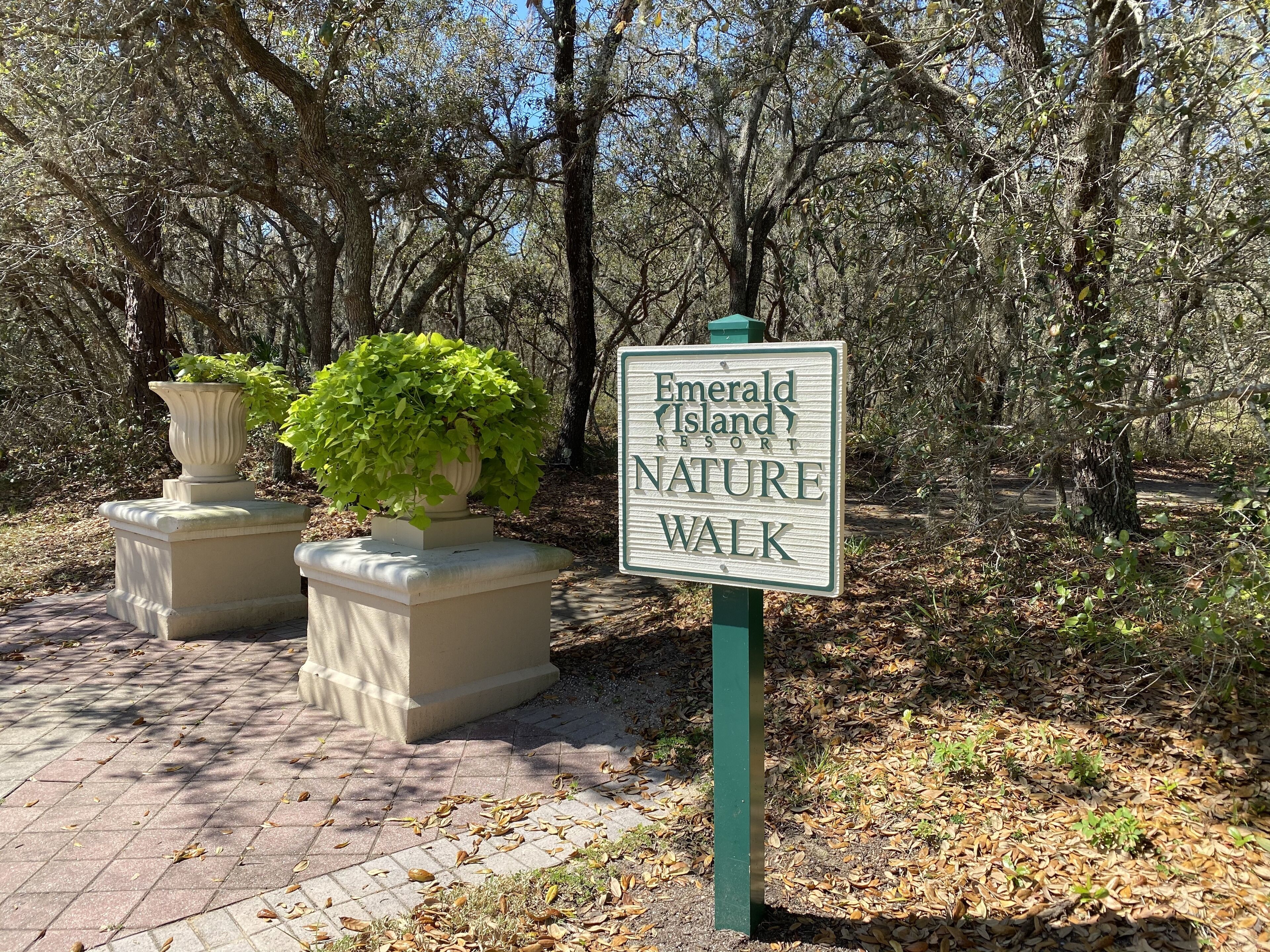 Un panneau indiquant le sentier de découverte de la nature du complexe hôtelier Emerald Island Resort, entouré d’arbres et bordé d’un chemin pavé.