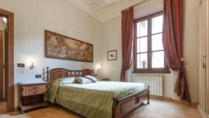A traditional bedroom with a wooden bed, a nightstand, a dresser, a large window with curtains, and a painting on the wall. - Il Battistero Apt - Luxury Apartments at 20 steps from Duomo; Elevator equipped. (Firenze)