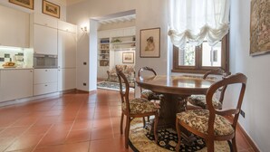 A dining area with a wooden table and chairs, a kitchen in the background, and a view through a window. - Il Battistero Apt - Luxury Apartments at 20 steps from Duomo; Elevator equipped. (Firenze)