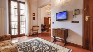 A spacious living room with a large window, a television, a chandelier, and a wooden cabinet. - Il Battistero Apt - Luxury Apartments at 20 steps from Duomo; Elevator equipped. (Firenze)