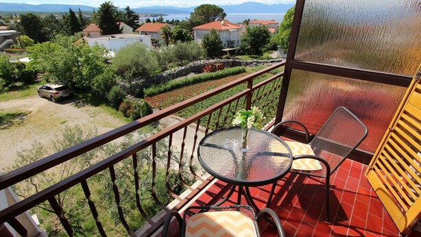 Un balcón con una mesa y sillas de vidrio, con vistas a una zona residencial con casas y una vista despejada del mar.