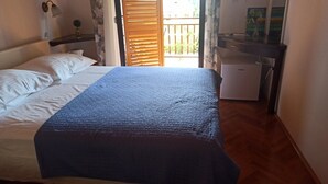 Un dormitorio con cama, un escritorio pequeño y ventana con vista a follaje.