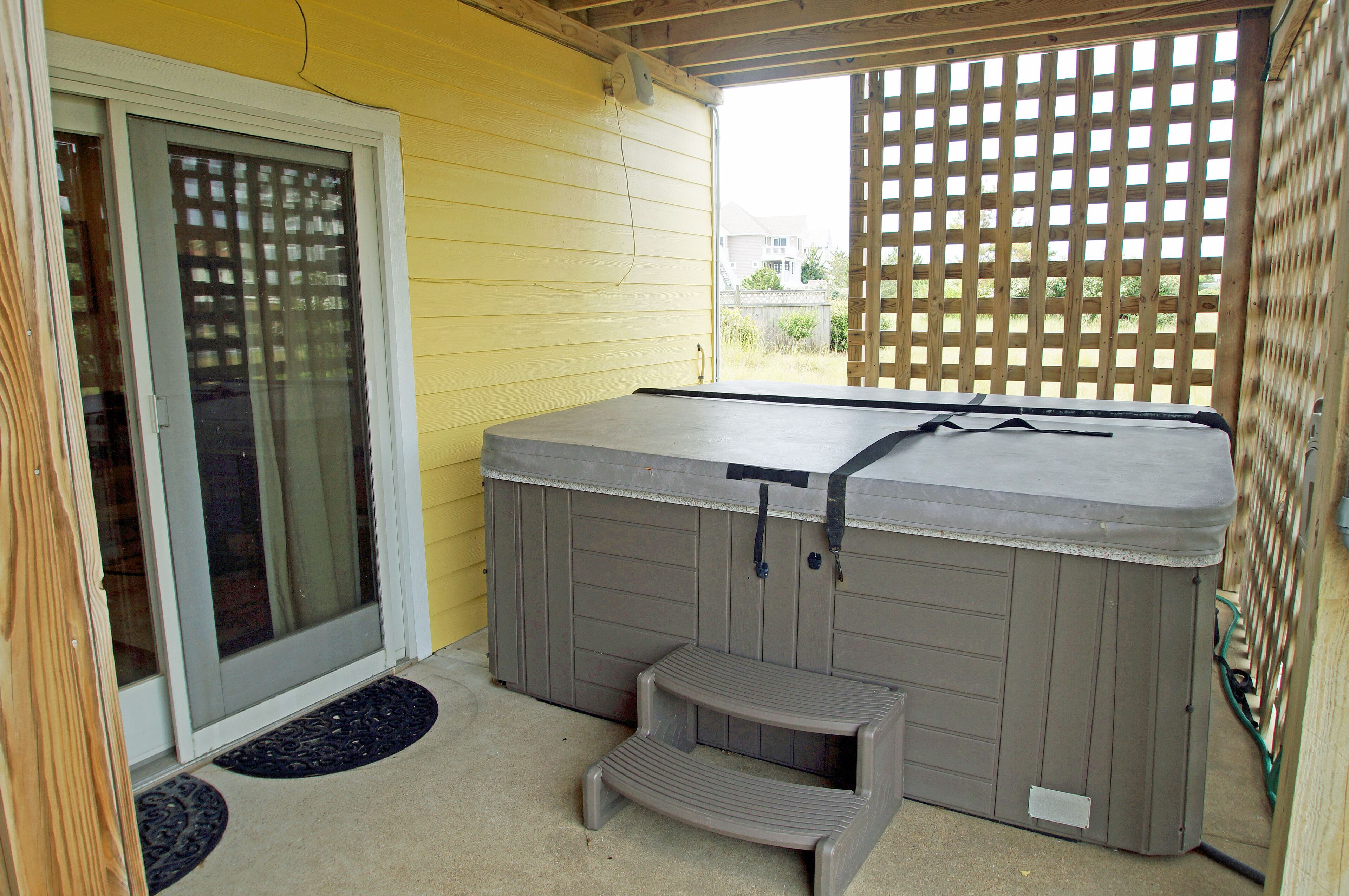 A hot tub with a step, a sliding glass door, and a wooden fence.