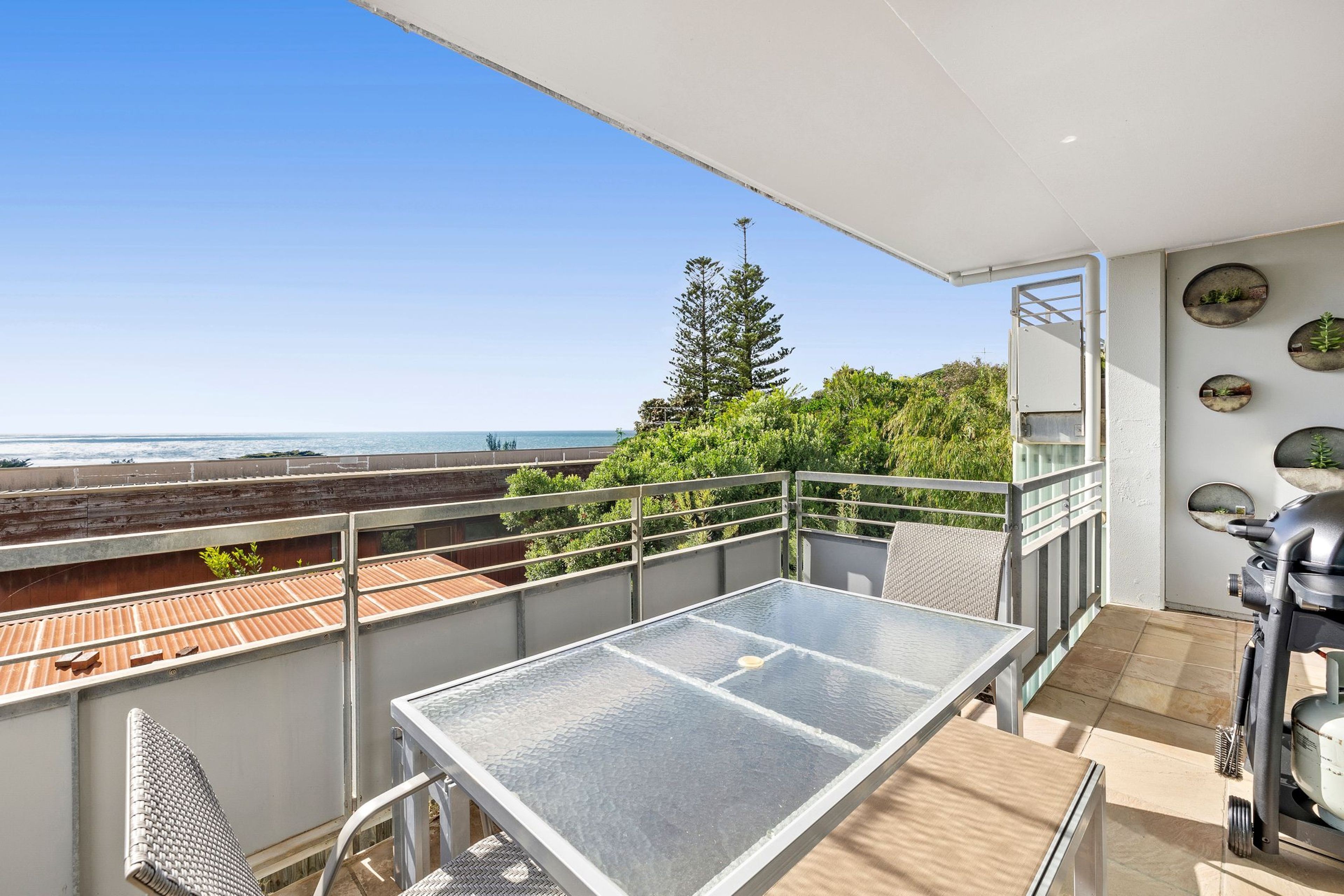 A balcony with a table and chairs, overlooking a beach and ocean.