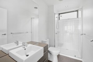 A modern bathroom with a dual sink, a toilet, and a glass-enclosed shower area. - Point Grey Apartment 7 (Lorne)
