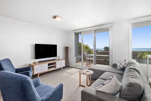 A modern living room with a flat-screen TV, a sofa, a chair, and a small table. - Point Grey Apartment 7 (Lorne)