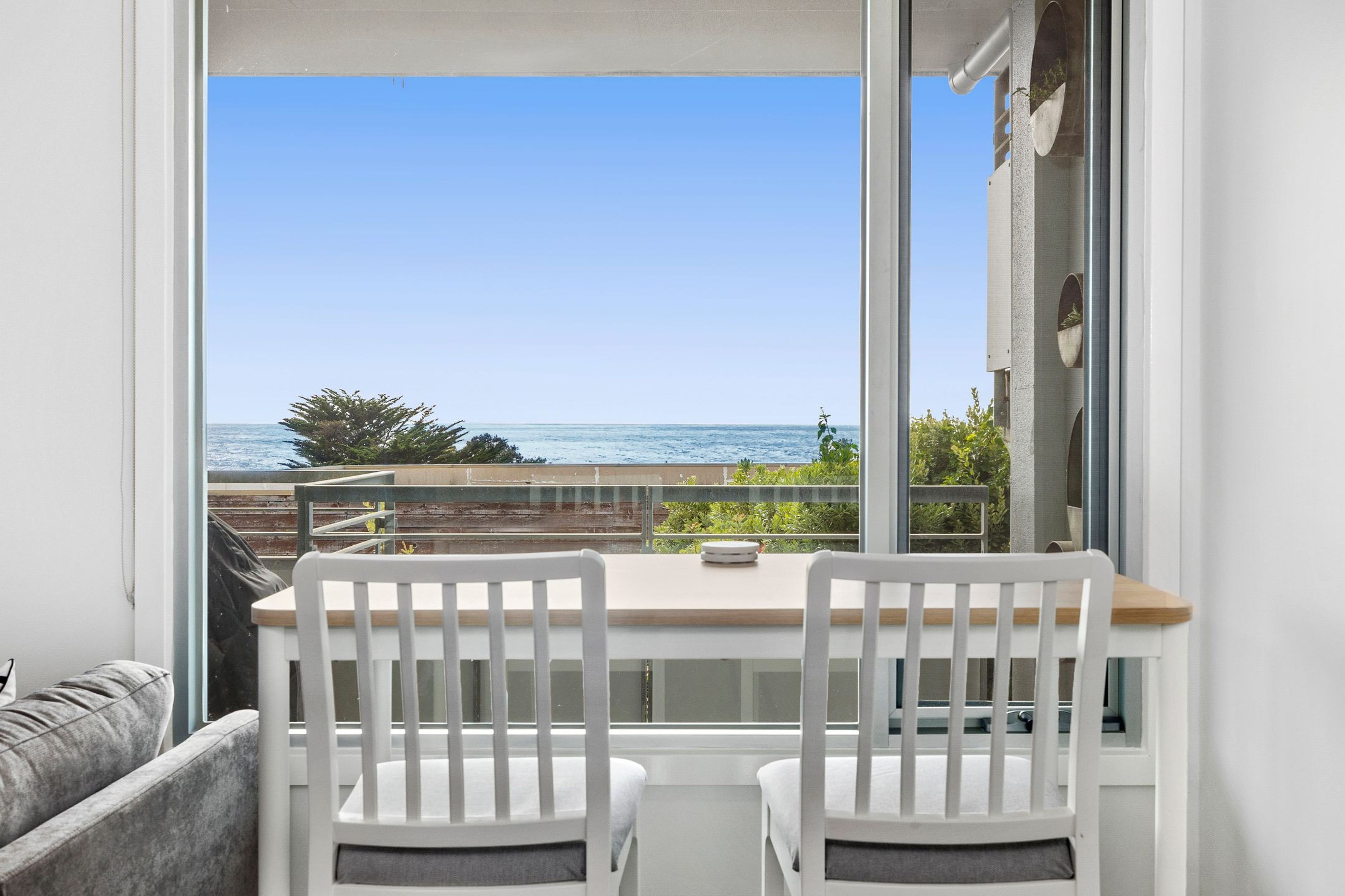 A balcony with two white chairs and a table, overlooking a clear blue sea and a distant coastline.