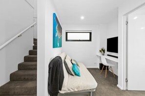 Ein modernes Interieur mit Treppe, einem Bett mit Kissen, einem Schreibtisch mit Computer und einem Fernseher.