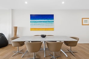 Ein Essbereich mit Tisch und Stühlen, ein Gemälde einer Strandansicht und ein gerahmtes Bild an der Wand.