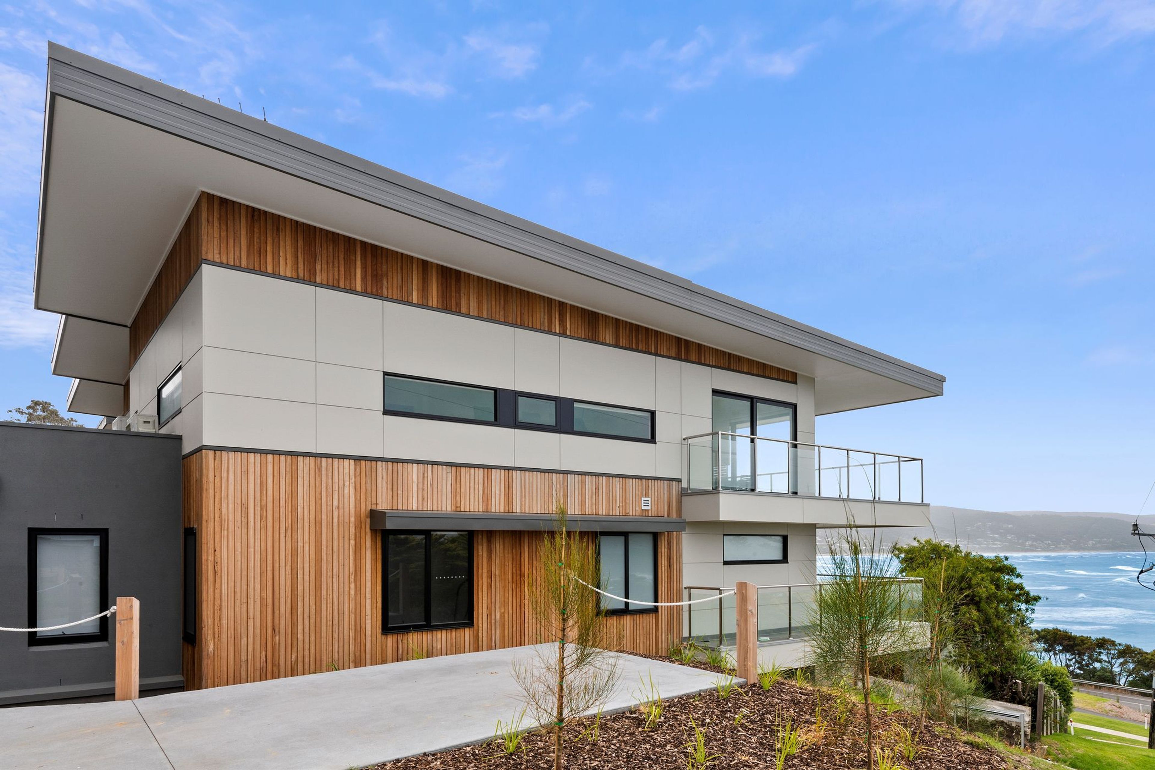 Een modern huis met twee verdiepingen, een balkon, grote ramen en uitzicht op zee.