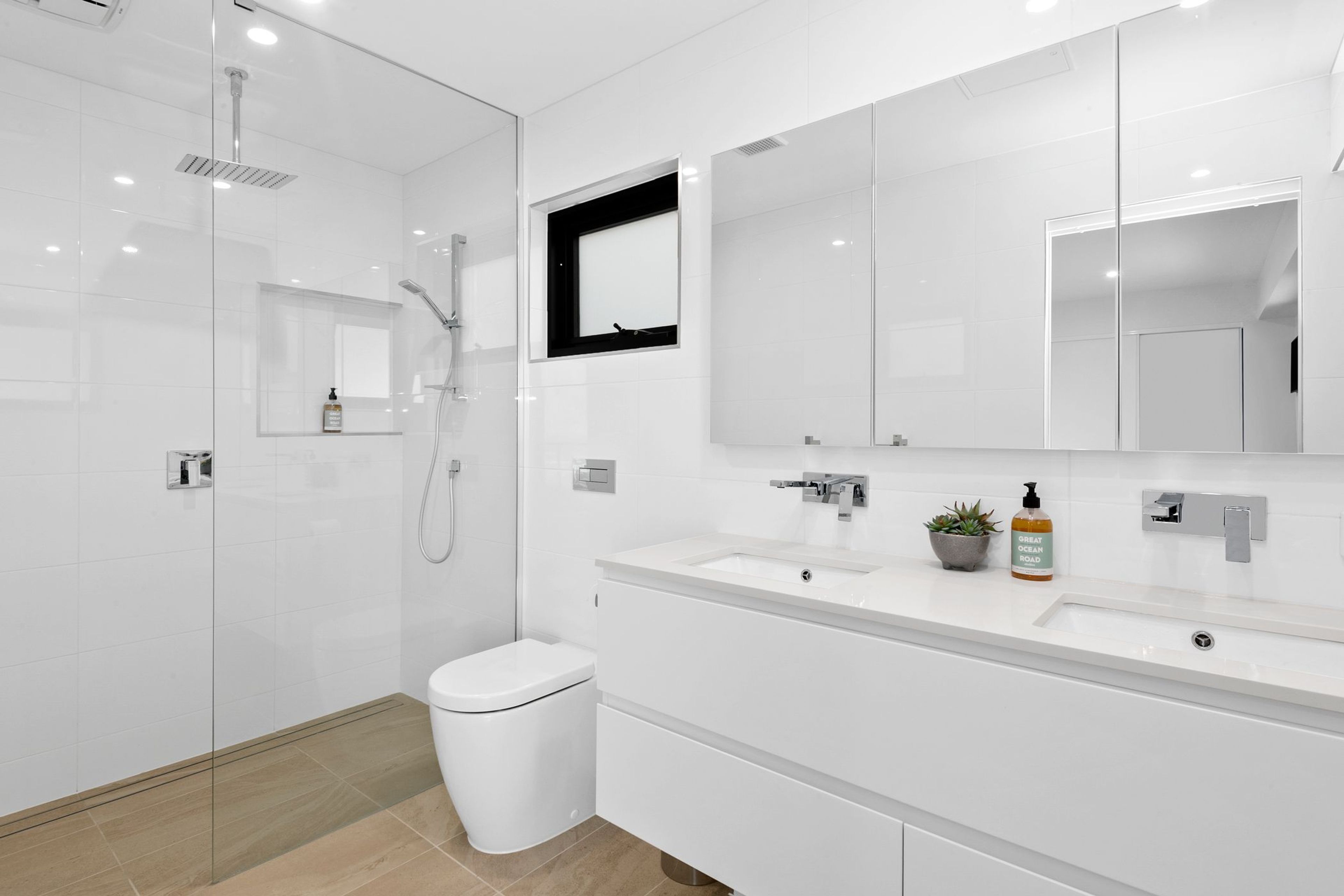Un baño moderno con ducha envuelta en vidrio, inodoro blanco y tocador con lavabo y espejo.