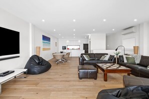 Un salon moderne doté d’un téléviseur à écran plat, de canapés en cuir, d’une table basse et d’un coin repas avec une table et des chaises blanches.