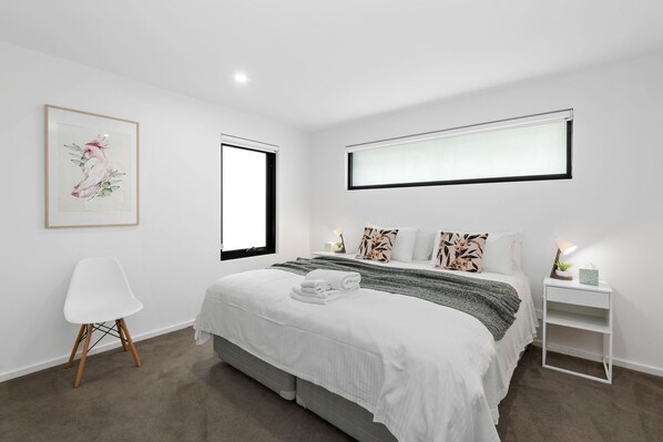A modern bedroom with a bed, bedside tables, a chair, and artwork on the wall. - Oceania 3 (Lorne)
