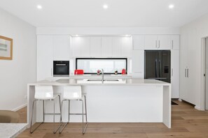 Une cuisine moderne avec des meubles blancs, un îlot central doté de tabourets de bar, un four noir, un grille-pain rouge et un réfrigérateur en acier inoxydable.