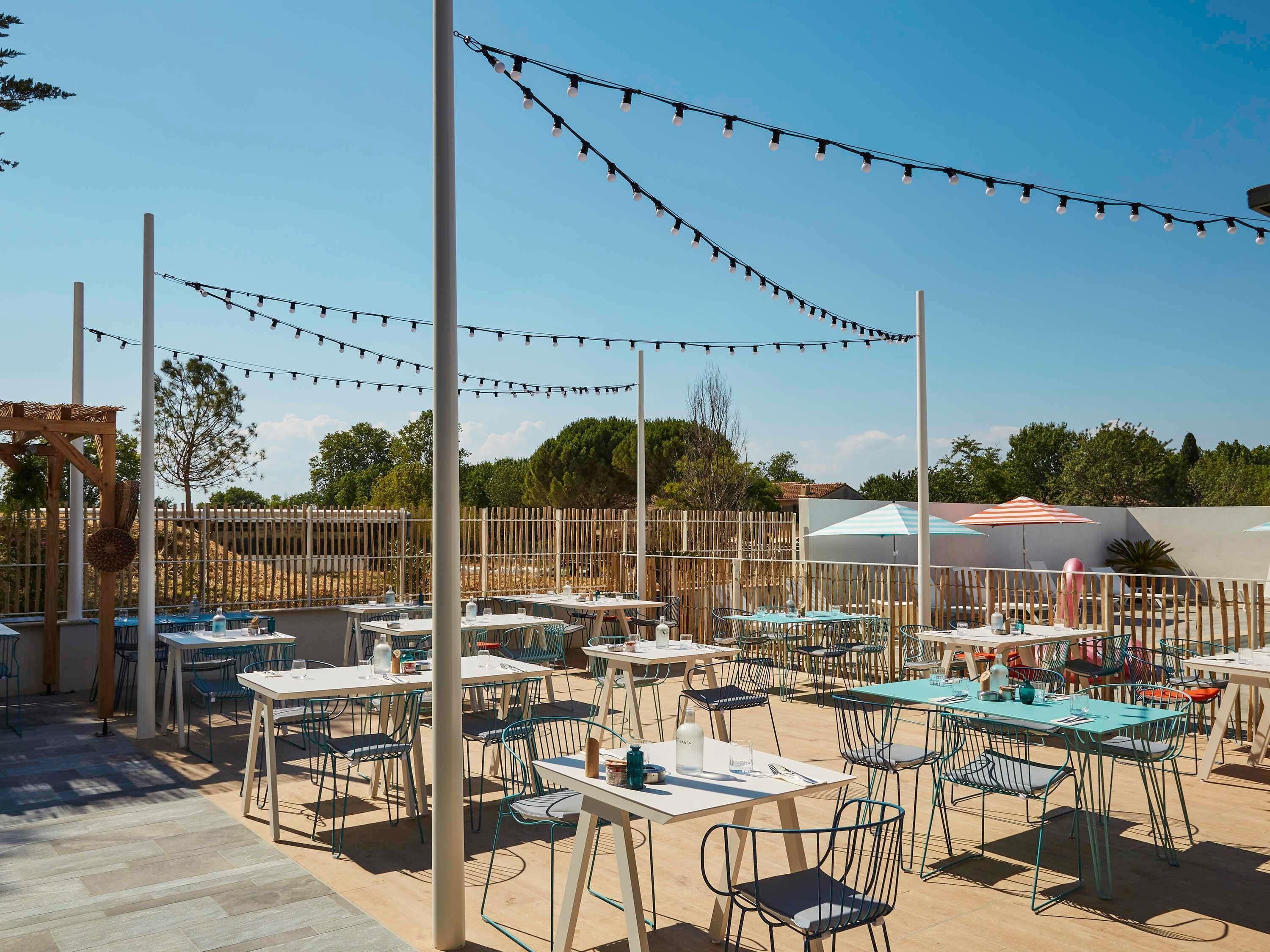 An outdoor dining area with tables and chairs, string lights, and a wooden fence.