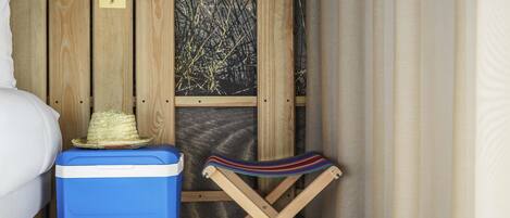 Habitación pequeña con una cama, un enfriador azul, un sombrero de paja y una toalla a rayas sobre una silla plegable de madera.