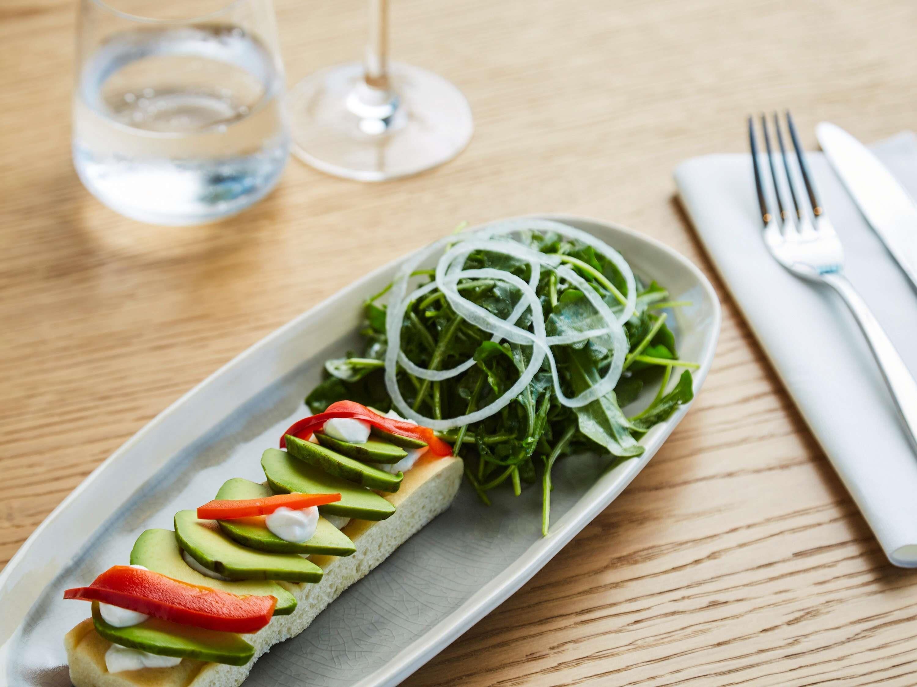 Ein Teller mit einem Sandwich und einem Beilagensalat auf einer Holztischplatte.
