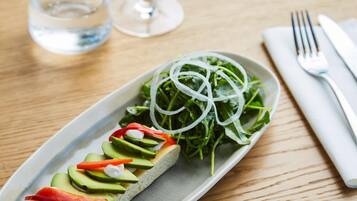 Ein Teller mit einem Sandwich und einem Beilagensalat auf einer Holztischplatte.