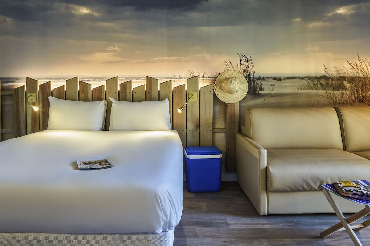 Ein Schlafzimmer mit einem Bett, einem kleinen blauen Mülleimer, einem Stuhl und einem Strohhut an der Wand.